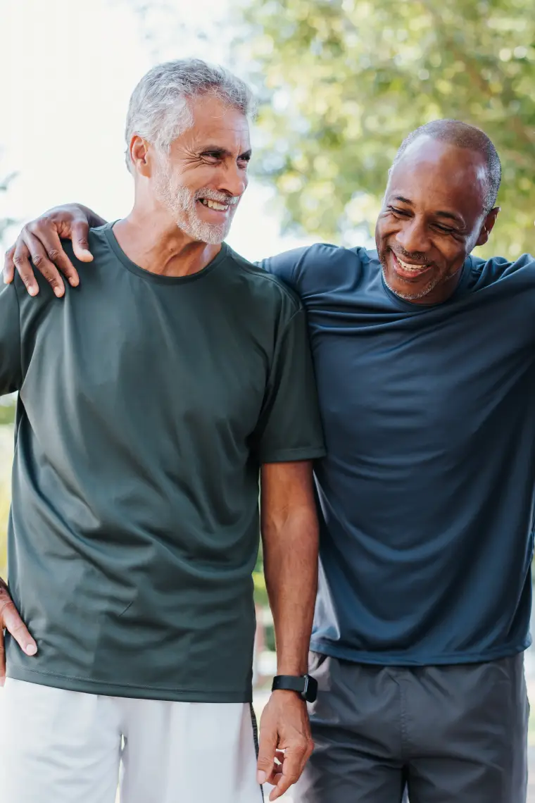 Two middle aged men smiling and walking outdoors together.